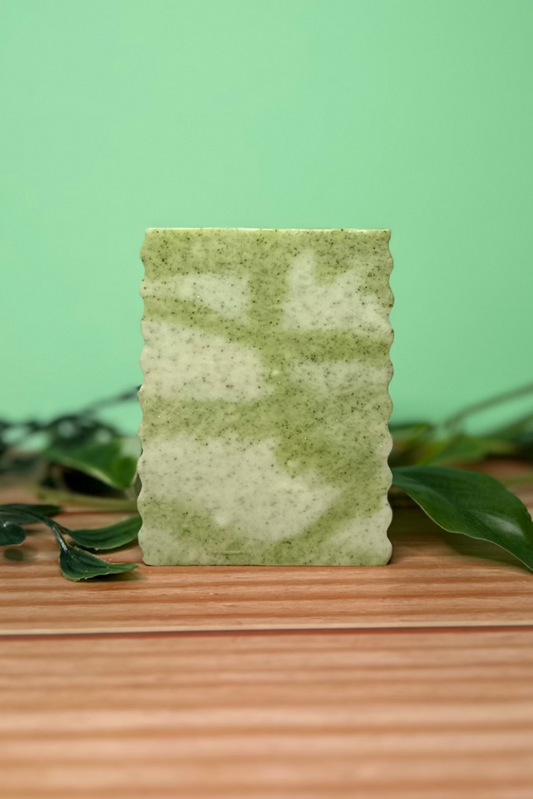 Green soap bar on a wooden surface with a green leafy background